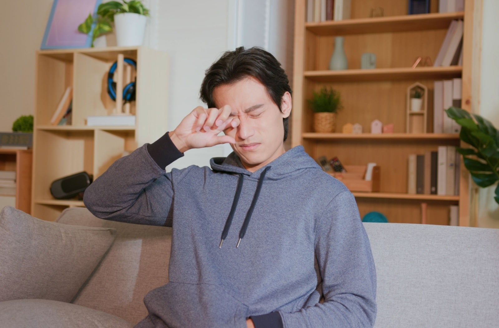 A man in a hoodie rubbing his eyes due to eye dryness.