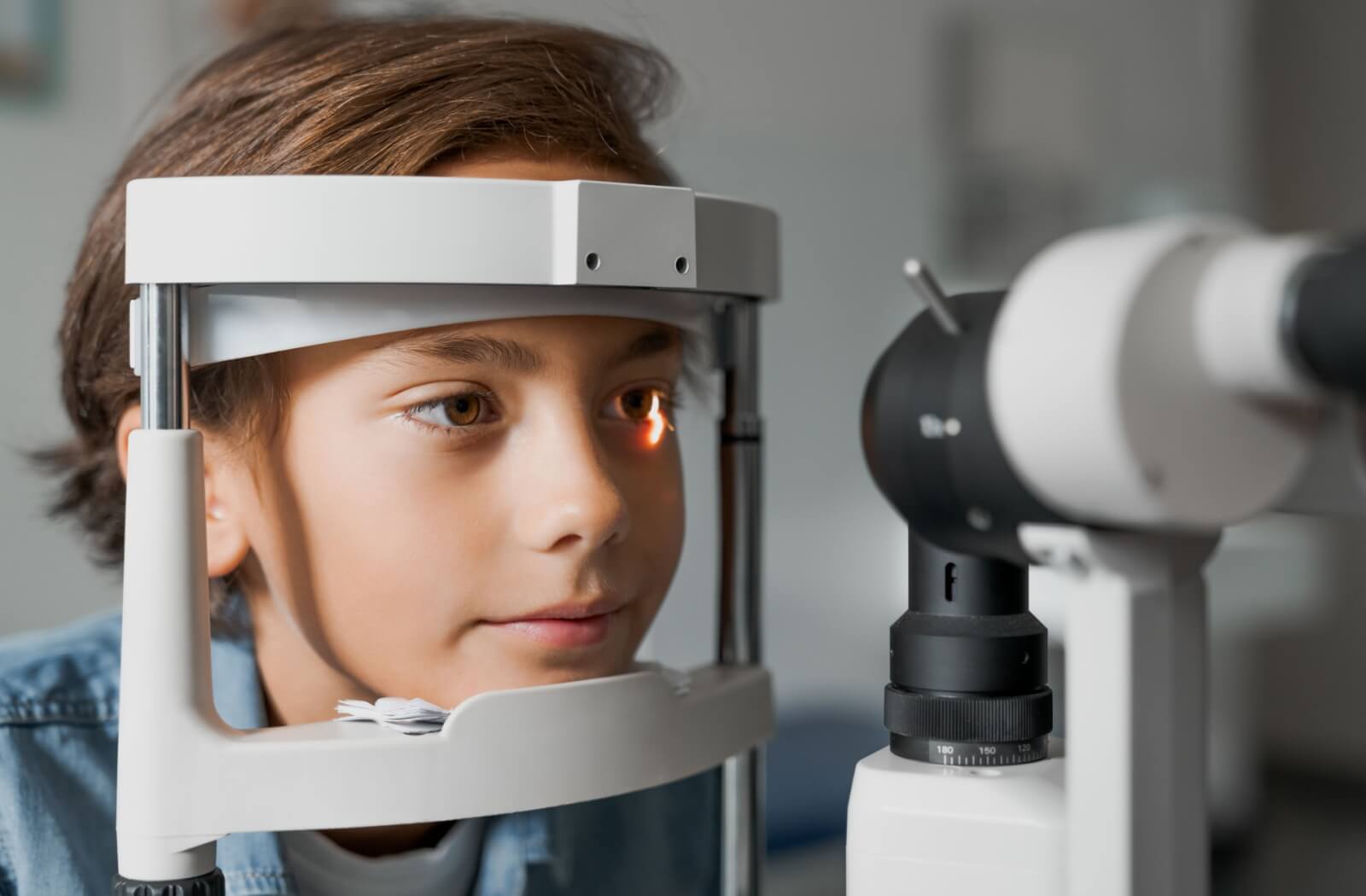A boy undergoes a slit lamp exam during an eye exam.