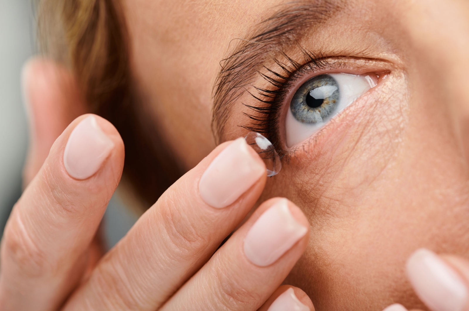 A close-up of a person putting a contact lens in their eye with their right middle finger.