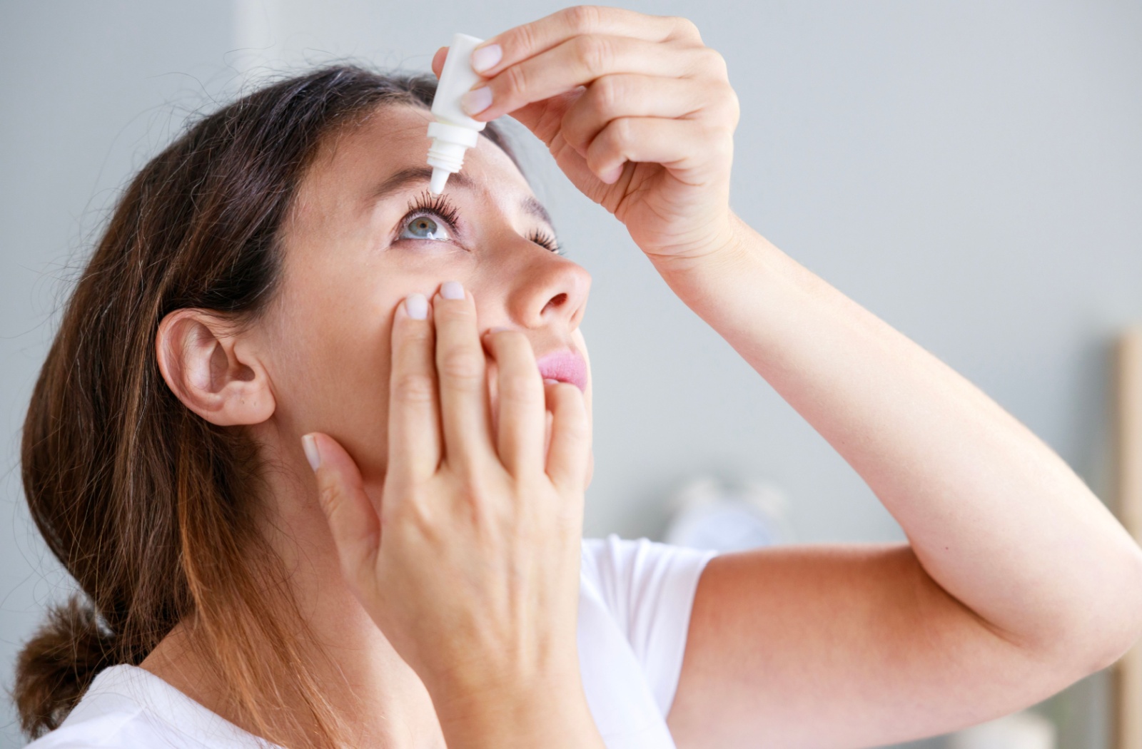 Person putting eye drops in their eye.