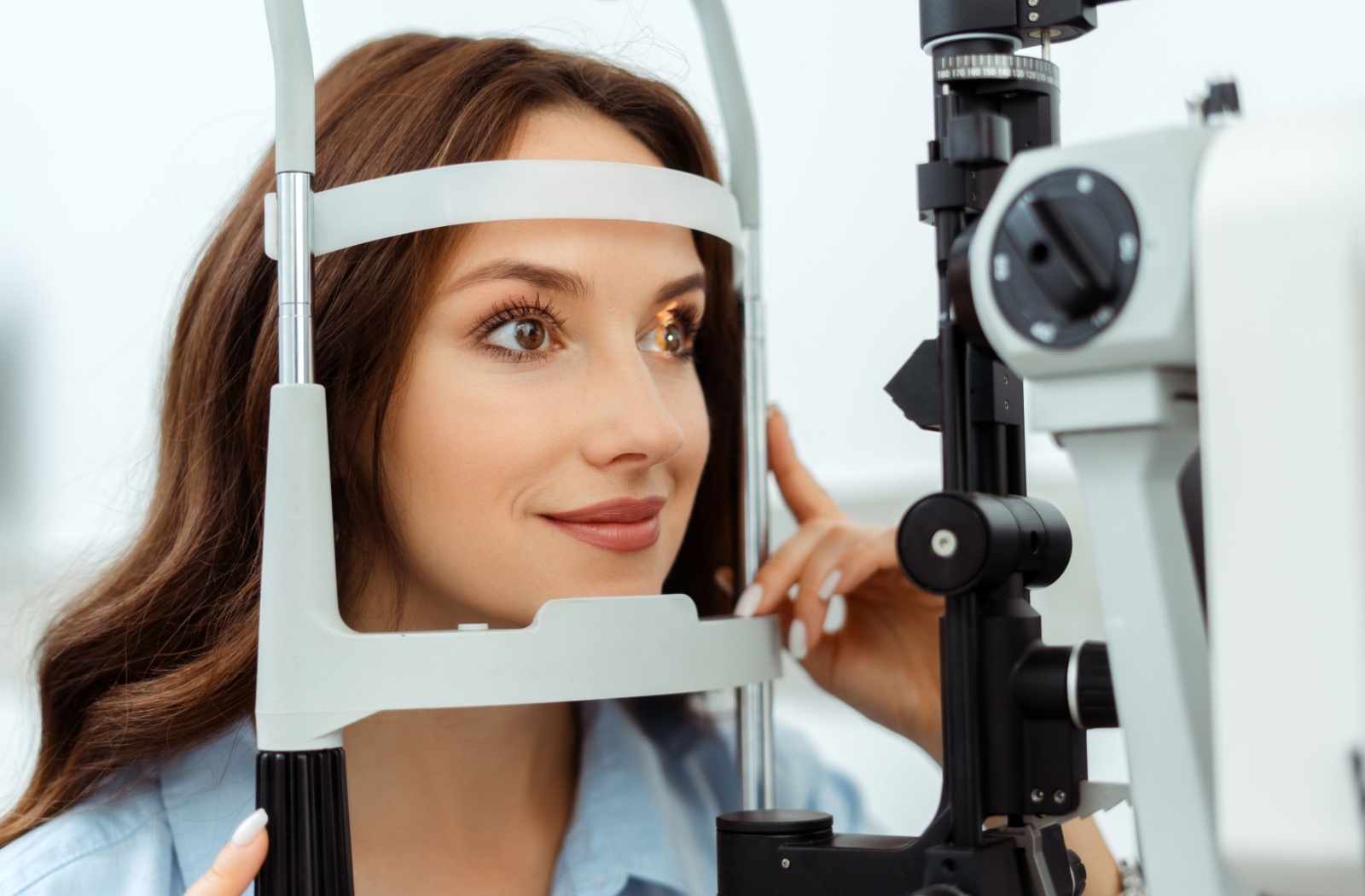 Smiling patient receiving an eye exam with a diagnostic laser tool directed at one eye.